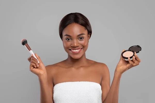 Senhora preta bonita feliz com pele perfeita faça maquiagem básica com cosméticos, mantenha o pó compacto e escova — Fotografia de Stock