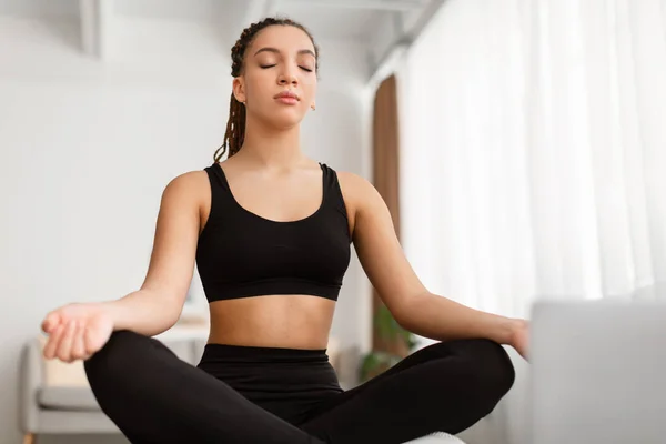 Rolig afrikansk amerikansk kvinde mediterer sidder gør yoga hjemme - Stock-foto