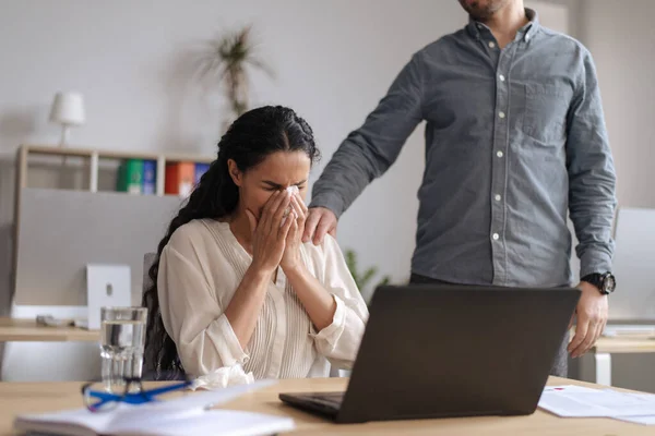 Aufgebrachte junge Frau weint neben Laptop im Büro, männlicher Kollege hilft und tröstet sie — Stockfoto