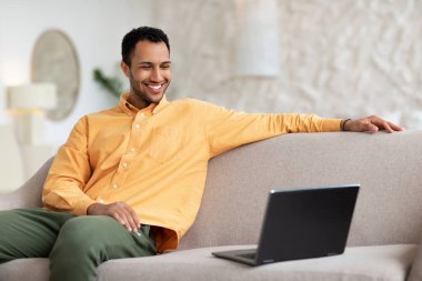 Bilgisayarda video izleyen, kanepede oturan gülümseyen genç adam.