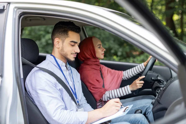 Ernstige duizendjarige Arabisch man neemt rijexamen van vrouw in hijab, dame aan stuurwiel rijden auto, profiel — Stockfoto