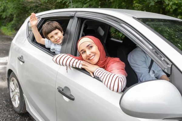 Щаслива арабська дружина в хіджабі і дитина махає руками у відкритому вікні в машині, чоловік на кермі — стокове фото