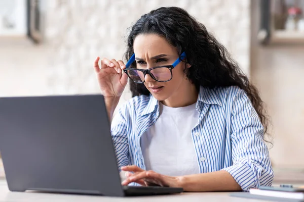 Problemas de visão. Latina senhora usando óculos enquanto trabalhava no computador portátil em casa, sentado na cozinha — Fotografia de Stock