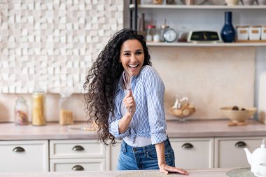 Evde tek başına eğlenmek. Hayali bir mikrofon gibi cihazda şarkı söyleyen, mutfakta dans eden mutlu bir kadın.