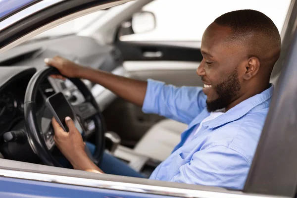 Szczęśliwy czarny człowiek za pomocą pokazano smartfon jazdy samochodem — Zdjęcie stockowe