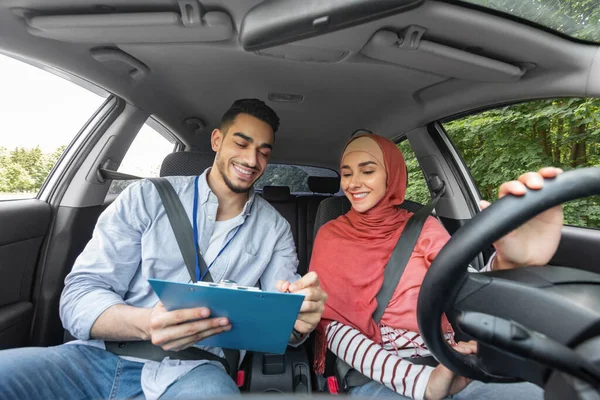 Happy millennial moslim guy instructeur geeft een uitstekend cijfer voor examen op de weg voor vrouw in hijab aan het stuur — Stockfoto