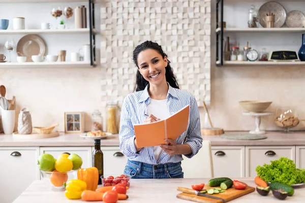 Concepto de alimentación saludable y dieta. Mujer emocionada haciendo lista de alimentos necesarios en la cocina, la celebración de cuaderno con pluma —  Fotos de Stock