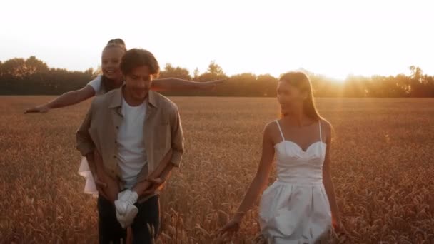 Bonito sorridente jovem família andando no campo de trigo no pôr do sol — Vídeo de Stock