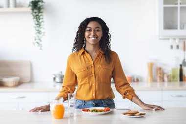 Neşeli siyah kadın düzgün kahvaltı yapıyor, mutfağın içinde.