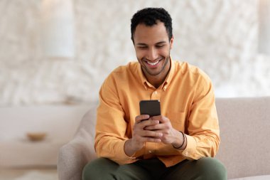 Evde akıllı telefon kullanan gülümseyen bir Arap portresi.