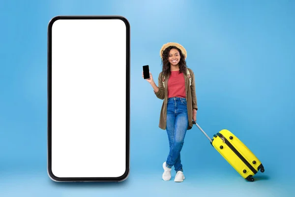 携帯電話の近くに立っているスマートフォンを示す黒の旅行者の女性、青の背景 — ストック写真