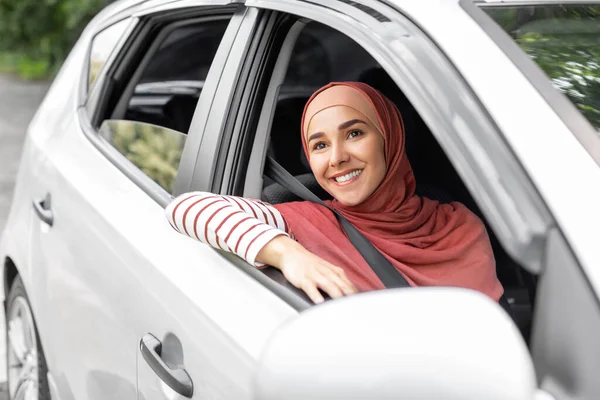 Vrolijke mooie duizendjarige Midden-Oosterse vrouw in hijab rijden in auto met chauffeur, kijkt uit open raam — Stockfoto