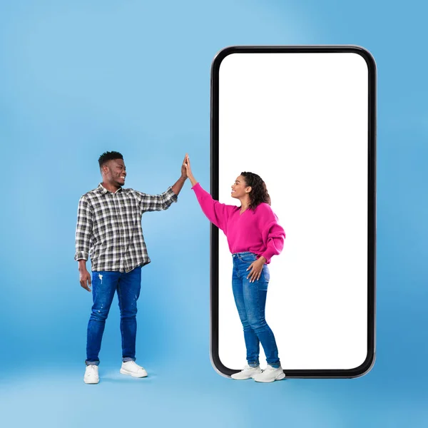 青い背景の上に高い5を与える携帯電話の近くのアフリカのカップル — ストック写真