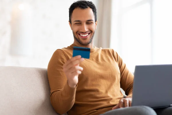 Casual χαμογελαστός άνθρωπος χρησιμοποιώντας το PC και την πιστωτική κάρτα στο σπίτι — Φωτογραφία Αρχείου