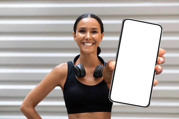 Jovem atleta feminina árabe feliz com fones de ouvido mostra smartphone grande com tela vazia — Fotografia de Stock