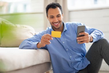 Gülümseyen adam evde telefon ve kredi kartı kullanıyor.