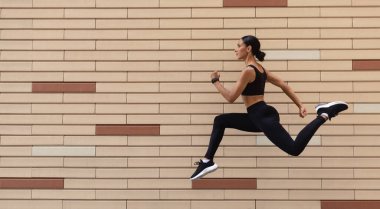 Spor giyim sektöründe ciddi genç Arap bayan sporcu. Duvarda, duvarda, profilde, panoramada donup kalmış.