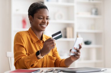 Akıllı telefon ve kredi kartı kullanan mutlu Afrikalı Amerikalı kadın.
