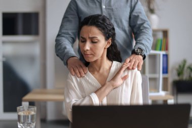 Erkek patron ellerini kadın sekreterlerin omuzlarına koyuyor, genç kadın ofisteki tacizden tiksiniyor.