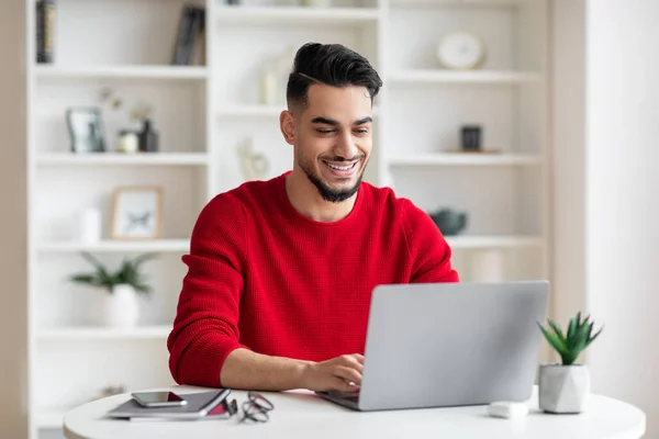 Fröhlich attraktiver arabischer Geschäftsmann mit Bart in roter Kleidung tippt auf Laptop im Home Office — Stockfoto