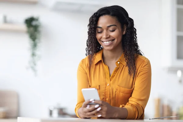 Mulher negra alegre usando novo smartphone em casa — Fotografia de Stock