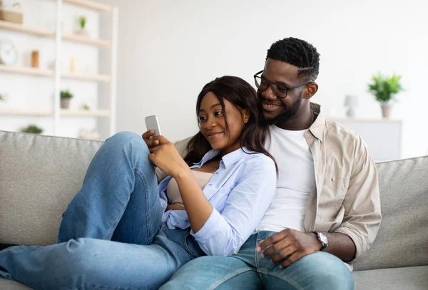 Αφροαμερικανό ζευγάρι κάθεται στον καναπέ, χρησιμοποιώντας το κινητό τηλέφωνο — Φωτογραφία Αρχείου