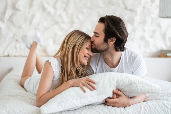 Affectueux jeune couple caucasien étreignant et embrassant au lit, exprimant l'affection à la maison — Photo