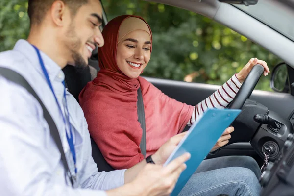 Sonriente hombre milenario de Oriente Medio, explicar las reglas, poner marca para la prueba de conducir para la mujer en hijab — Foto de Stock