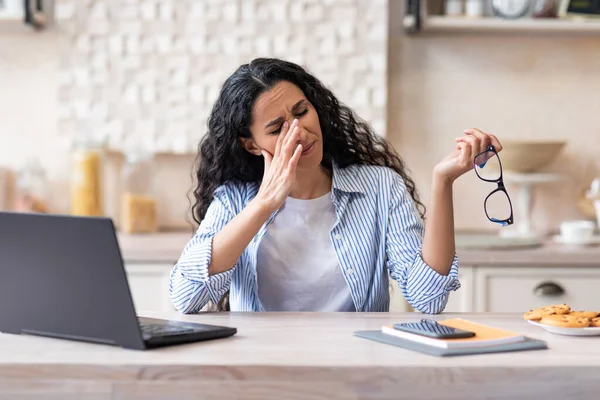 Ögontrötthet koncept. Frilansare dam trött efter att ha arbetat på laptop i köket interiör, kvinna som tar av glasögon — Stockfoto