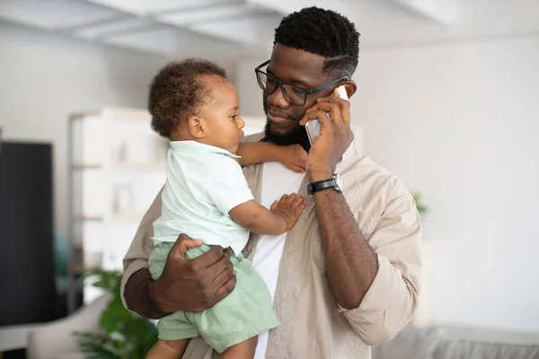 Negro padre hablando en celular celebración bebé en manos — Foto de Stock