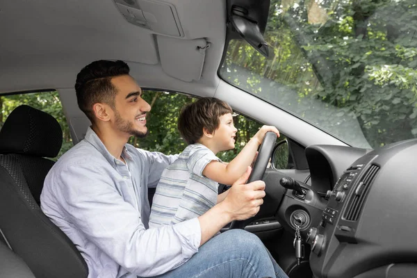 Gülümseyen genç adam yazın küçük bir çocuğa araba sürmeyi öğretiyor, direksiyonu tutuyor ve yola bakıyor, profil çıkarıyor. — Stok fotoğraf