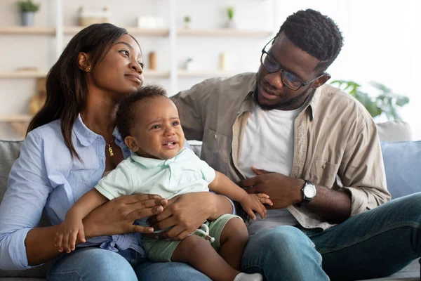 Афроамериканские родители утешают плачущего ребенка на диване — стоковое фото