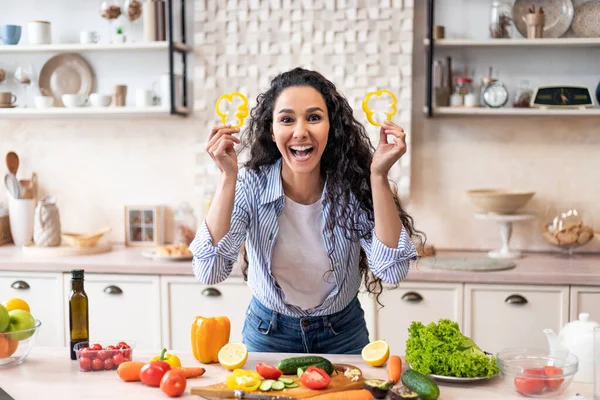 Mujer alegre divirtiéndose con vasos de pimiento dulce, jugando con la comida y jugando, cocinando ensalada en la cocina — Foto de Stock