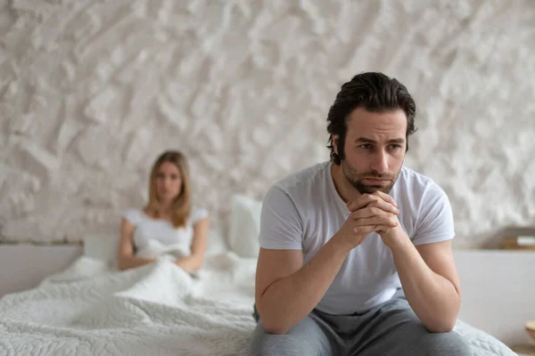 Young Caucasian man feeling upset, sitting on bed at home, not speaking to his offended wife after fight — Stock Photo, Image