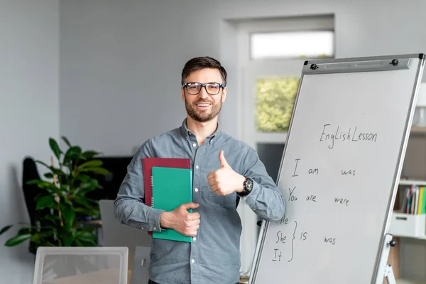 Positivo maduro masculino professor mostrando polegar até pé perto blackboard, recomendando novo on-line línguas estrangeiras escola — Fotografia de Stock