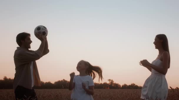 Семейные мероприятия. Счастливые молодые люди и дочь-подросток играют с мячом на свежем воздухе — стоковое видео