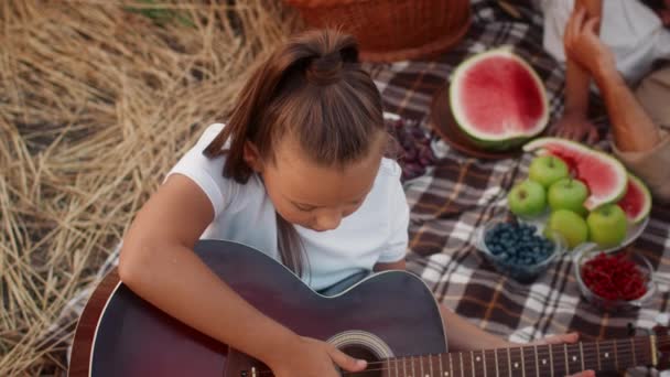Linda chica adolescente tocando la guitarra en picnic familiar al aire libre en el campo de trigo — Vídeo de stock