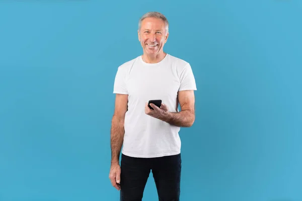 ชายผู้ใหญ่ที่มีความสุขใช้โทรศัพท์มือถือของเขาที่สตูดิโอสีฟ้า — ภาพถ่ายสต็อก