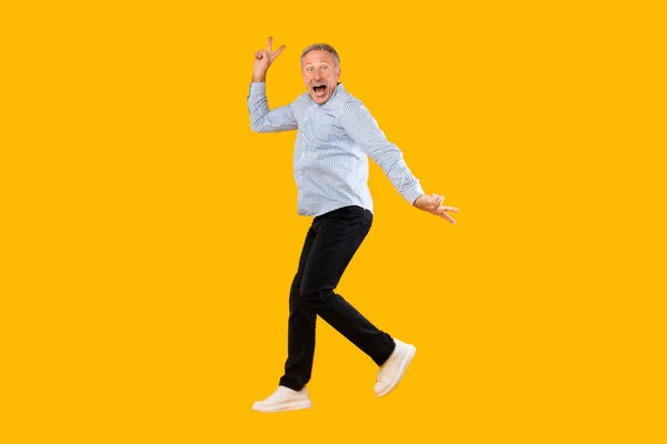 Opgewonden volwassen man springen in geel oranje studio — Stockfoto