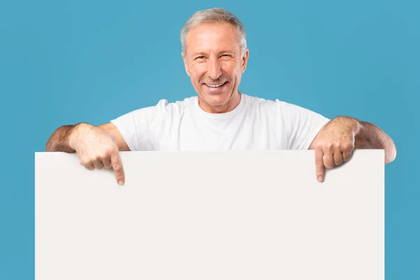 Felnőtt férfi kukucskál ki üres fehér hirdetőtábla a stúdióban — Stock Fotó