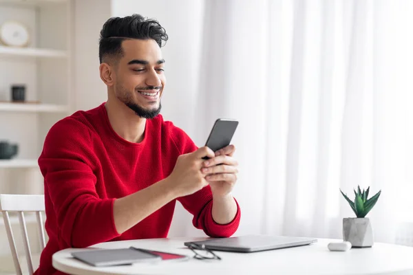 快乐迷人的阿拉伯年轻人，留着红胡子，在工作场所的智能手机上输入消息 — 图库照片