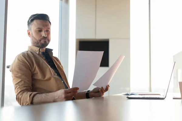 Вдумчивый бизнесмен читает деловые документы, хранящие документы, находящиеся в офисе — стоковое фото
