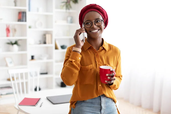 Cheerful young black woman talking on phone, having coffee break — Stock Photo, Image