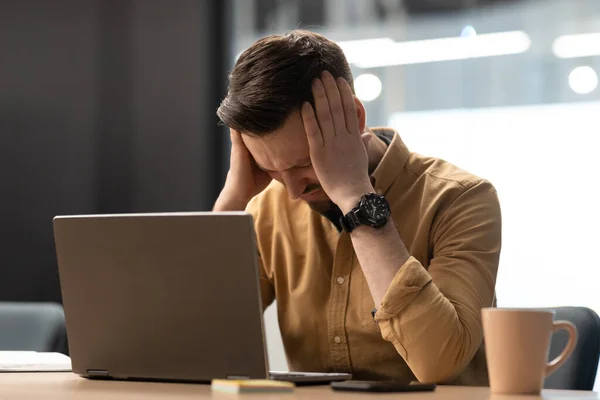 Infeliz hombre de negocios cerca del ordenador portátil tocando la cabeza tener dolor de cabeza en la oficina — Foto de Stock