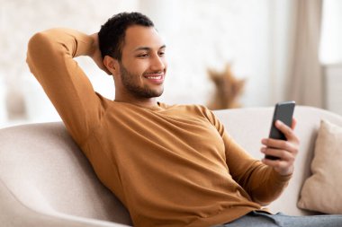 Evde akıllı telefon kullanan gülümseyen bir Arap portresi.