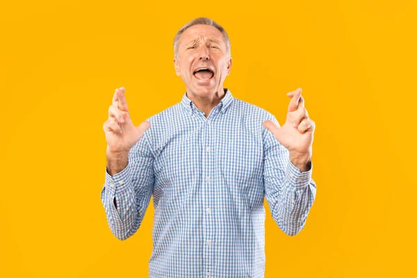 Hopeful senior man crossing his fingers making wish — Stock Photo, Image