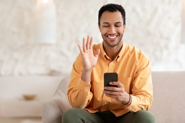 Smiling young man waving hand using mobile phone — ストック写真