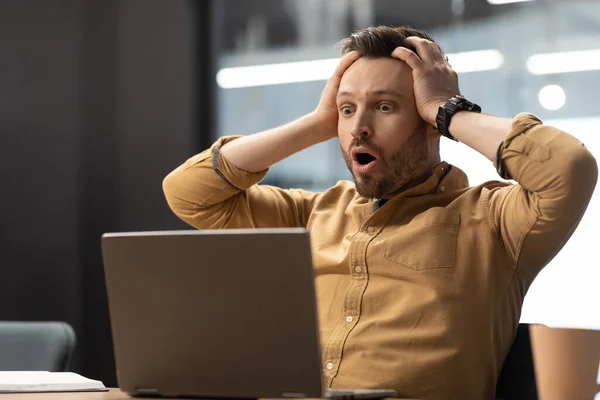 Empresario tocando la cabeza mirando al ordenador portátil en shock en la oficina —  Fotos de Stock