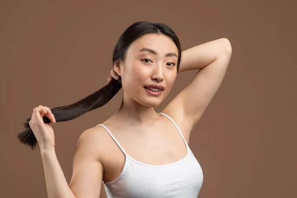 Jovem coreana com pele perfeita mostrando seu longo cabelo liso sedoso, posando no fundo do estúdio marrom — Fotografia de Stock