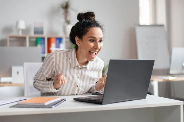 Ganhar. Empresária emocionada celebrando o sucesso, sacudindo punhos apertados e olhando para o laptop no escritório — Fotografia de Stock